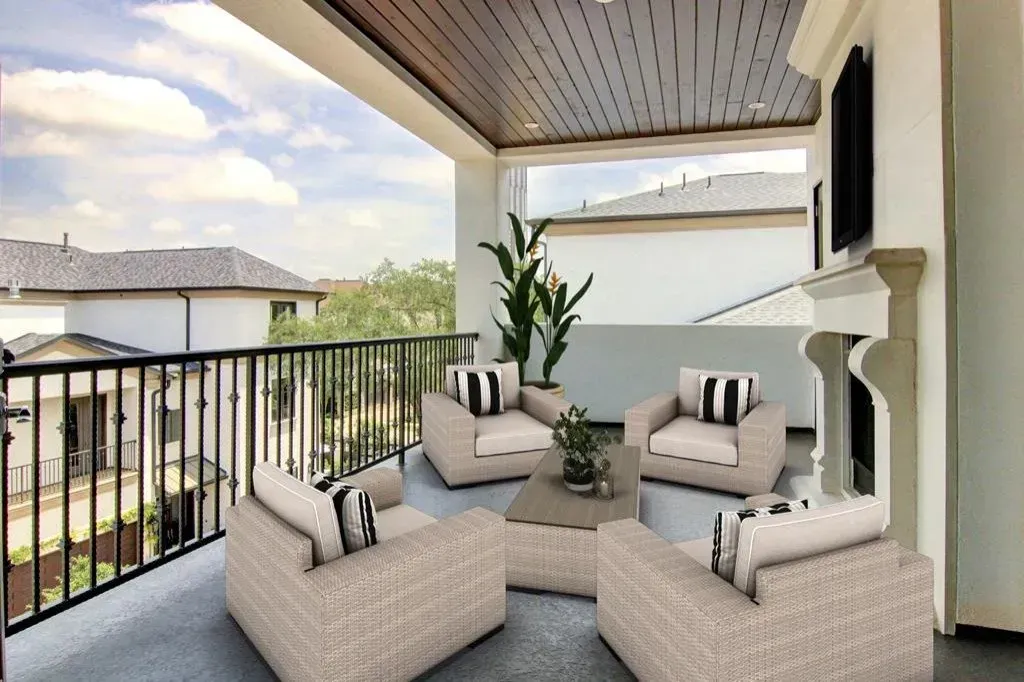 Outdoor patio with seating area, fireplace, and railing overlooking neighborhood on a sunny day.