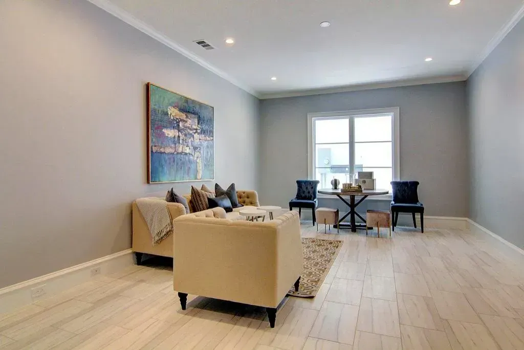 Living room with beige furniture, art, table, chairs, and window with light gray walls and white trim.