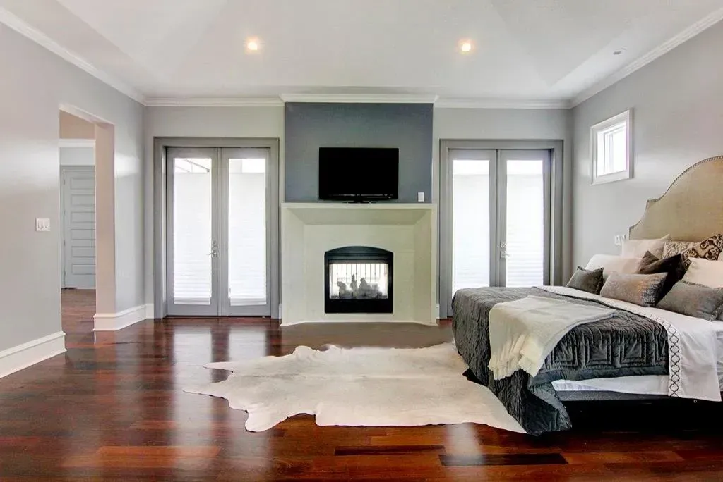Spacious bedroom with fireplace, TV, and large bed, hardwood floors, and gray walls.