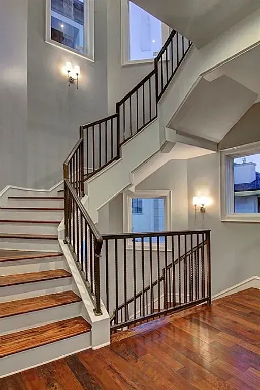 Wooden staircase with brown railing in a gray painted entry. Windows and sconces are visible.