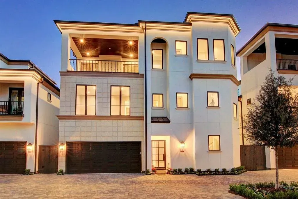Three-story white house with a balcony and garage, lit up at dusk.
