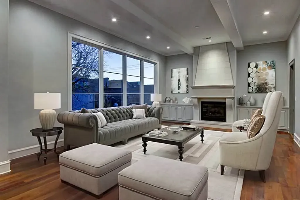 Living room with a tufted gray sofa, fireplace, large windows, and neutral decor.