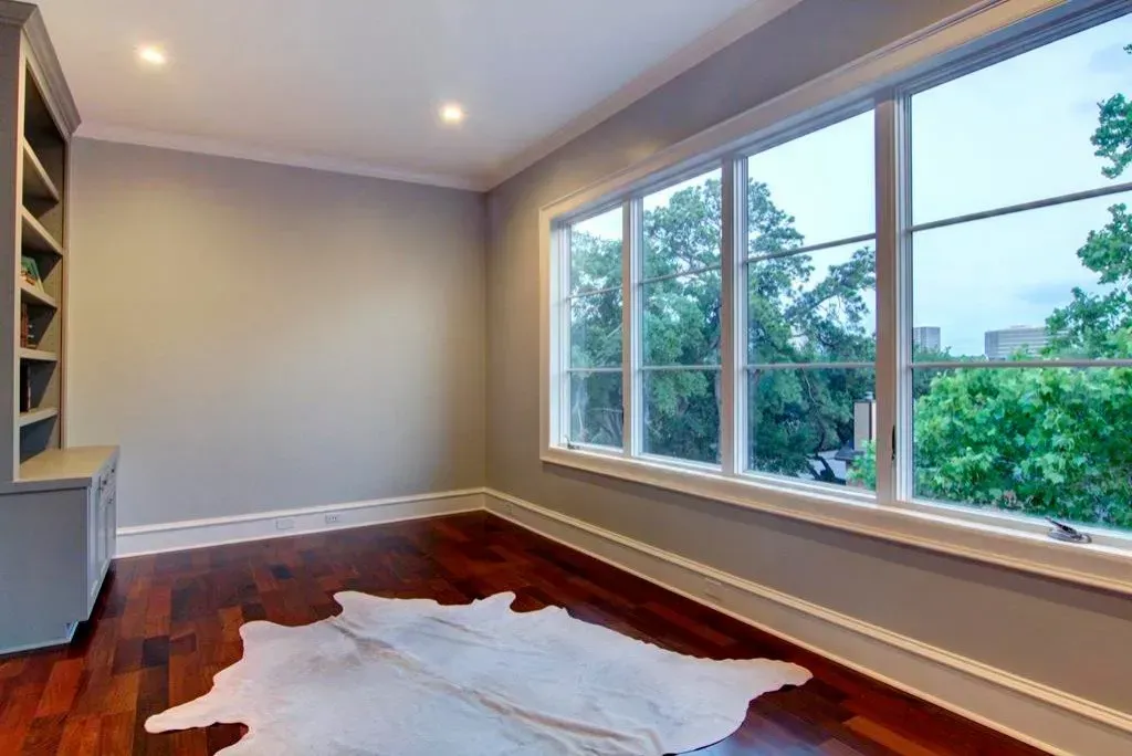Empty room with hardwood floors, built-in shelving, large windows with a view of trees, and a cowhide rug.