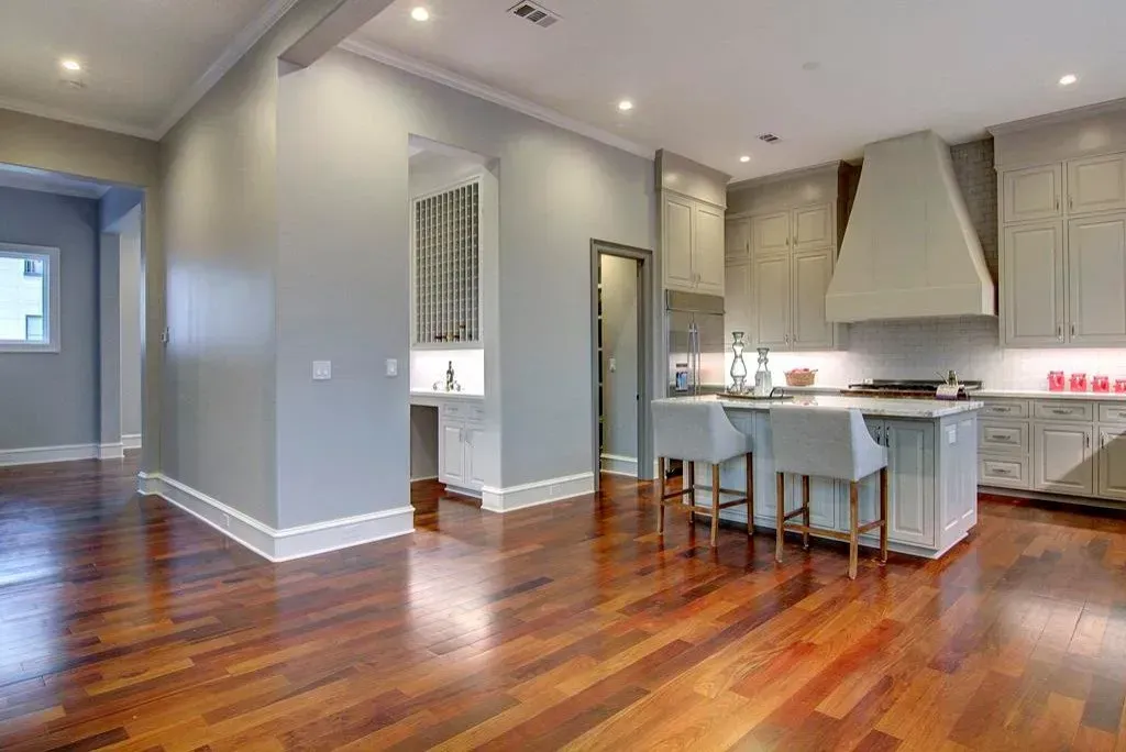 Spacious kitchen with wood floors, gray cabinets, island with stools, and an alcove with a wine rack.