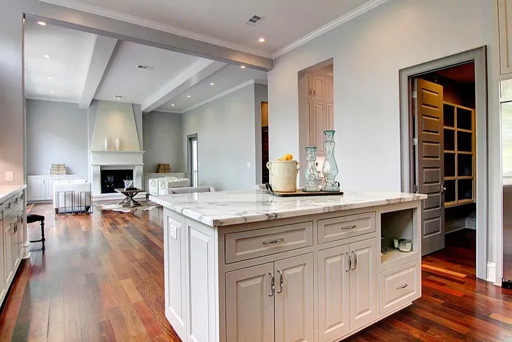Spacious kitchen with a marble-topped island, wooden floors, and a view of a living room with a fireplace.