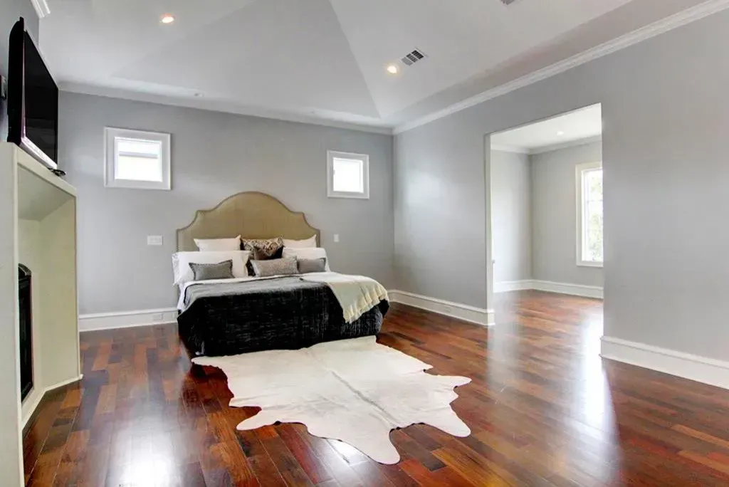 Bedroom with gray walls, hardwood floor, bed with cowhide rug, and an adjacent room.