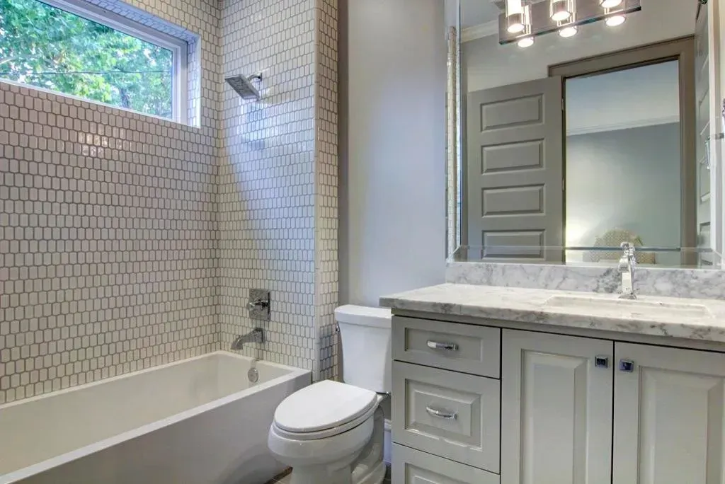 Modern bathroom with white tub, toilet, vanity, and shower, with patterned tile wall and large mirror.