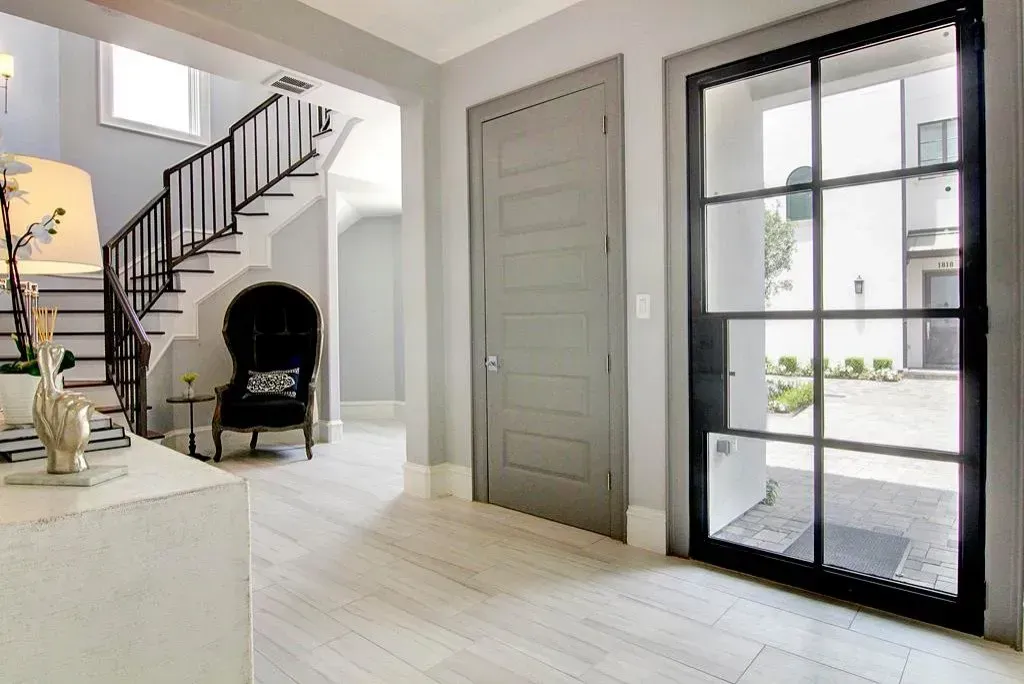 Entryway with gray walls, light wood floors, staircase, black iron door frame, and glass door.