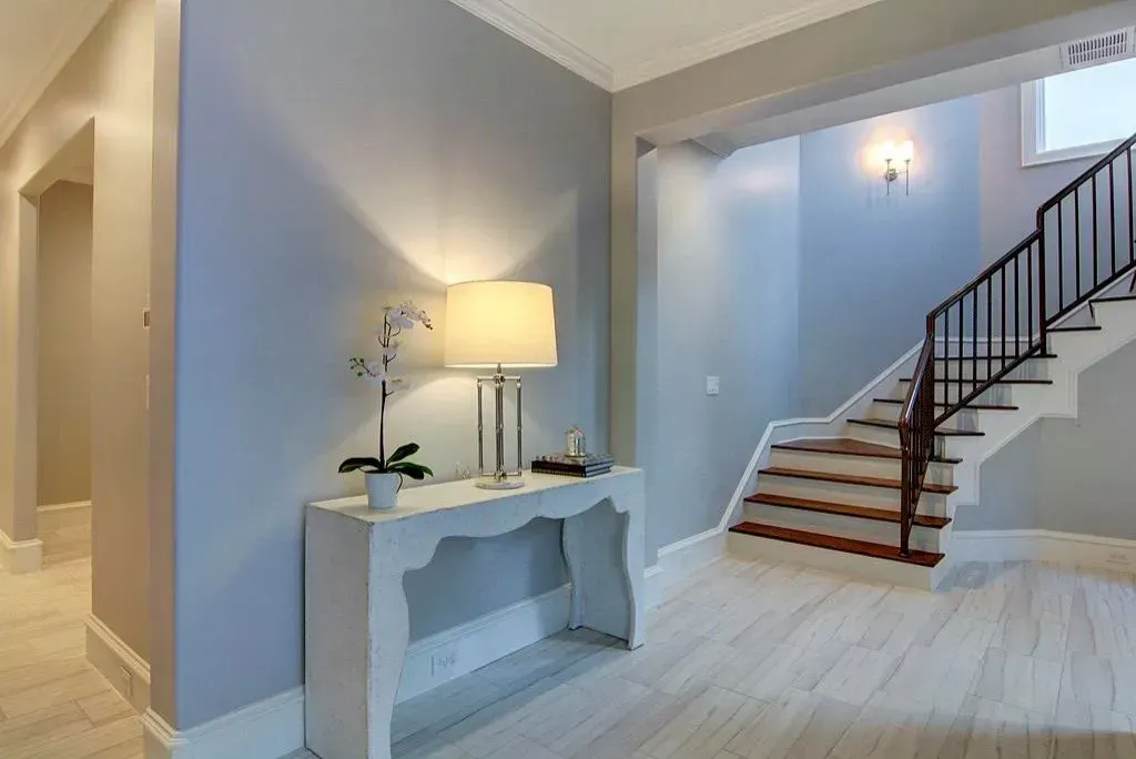 Light blue foyer with white table, lamp, staircase, and light wood floors.