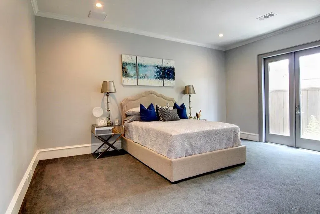 Bedroom with a bed, nightstands, artwork, and glass doors to an outdoor area. Gray walls and carpet.