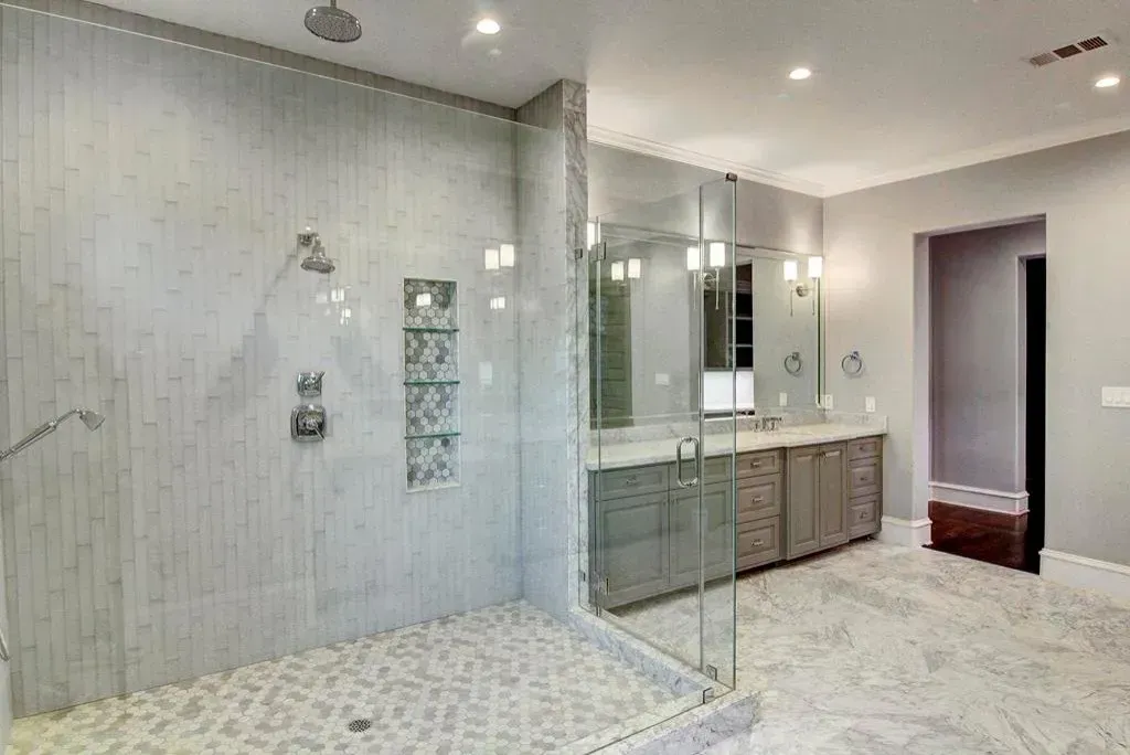 Spacious gray and white bathroom with a large glass-enclosed shower, dual vanity, and light gray cabinetry.