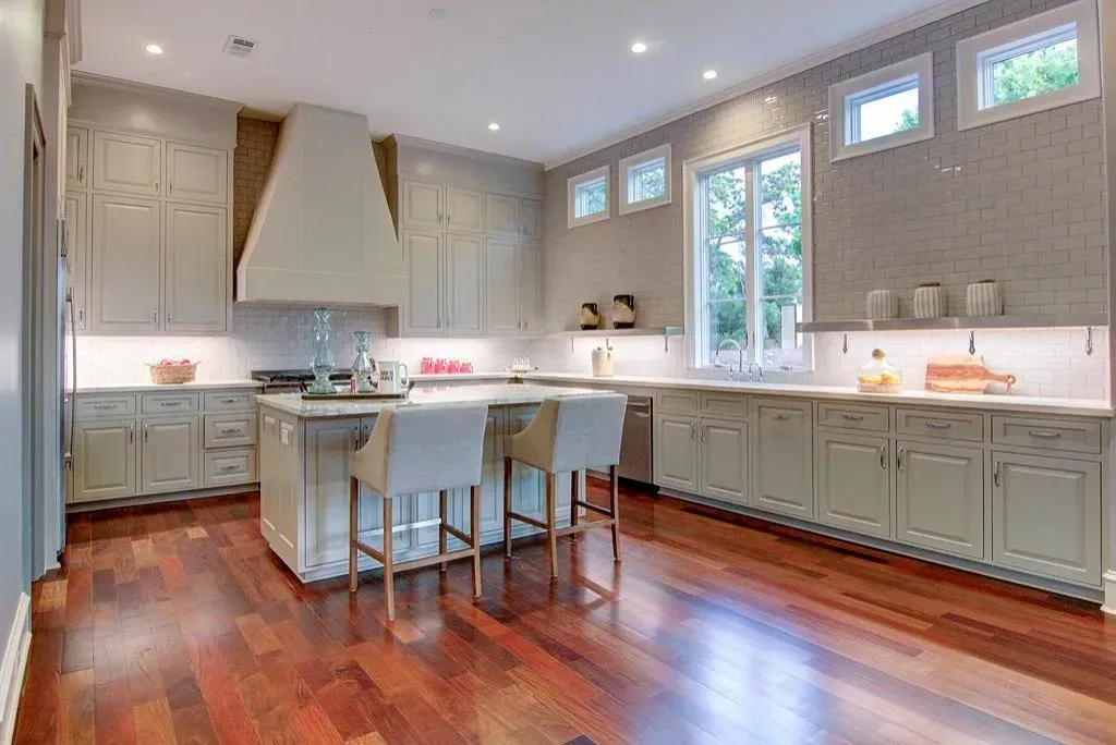 Spacious, modern kitchen with light green cabinets, wood floors, and an island with stools.