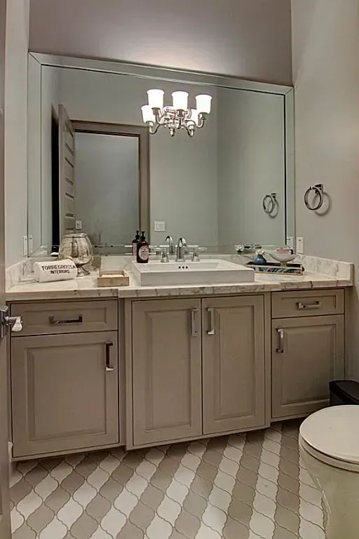 A bathroom with a white sink, vanity with cabinets, large mirror, and patterned floor.