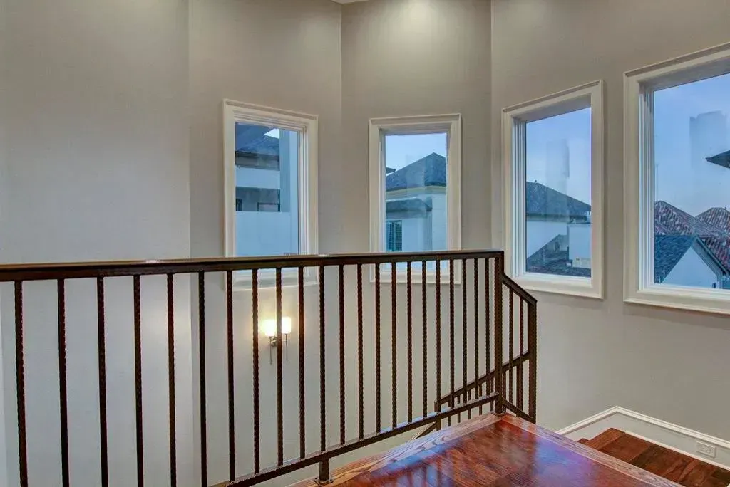 Staircase landing with brown railing, hardwood steps, and three windows overlooking rooftops.