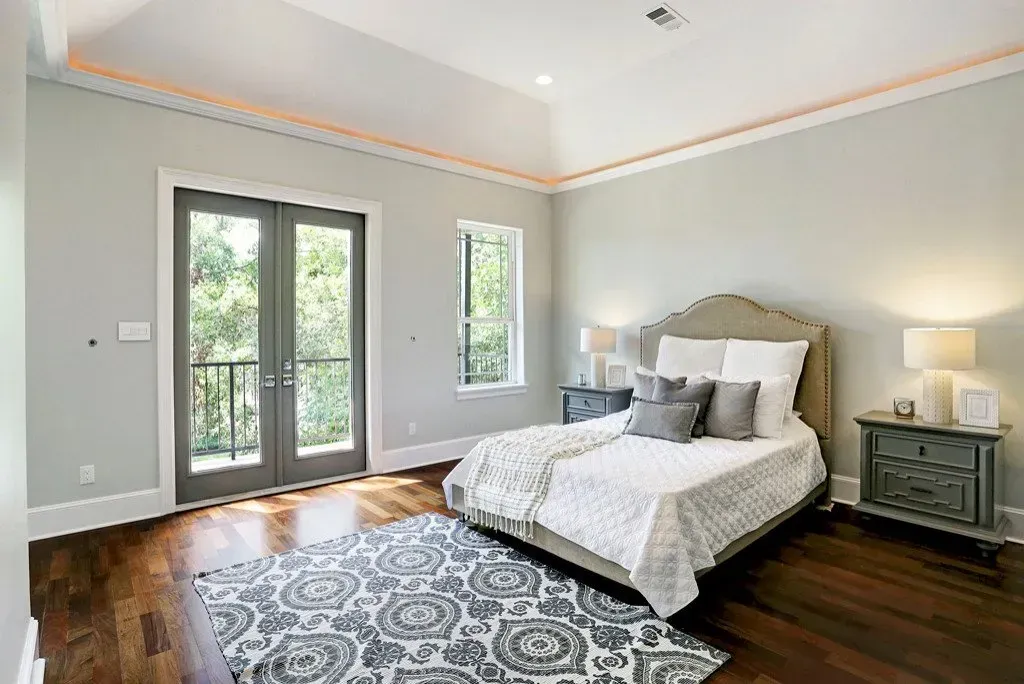 Bedroom with bed, dark wood floor, large doors to balcony, light blue walls, grey rug.