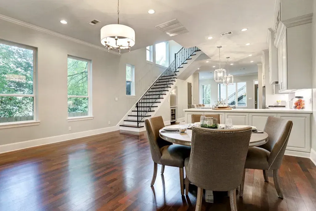 Dining room with wooden floor, round table, chairs, and a staircase.