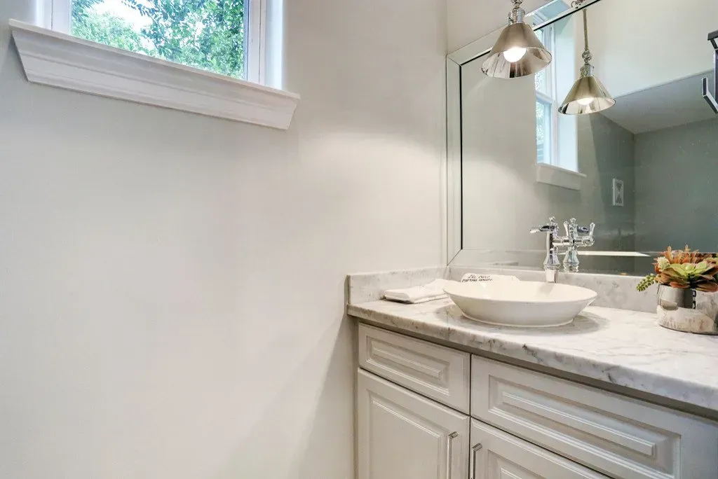 Bathroom with white cabinets, marble countertop, round sink, mirror, and two pendant lights.