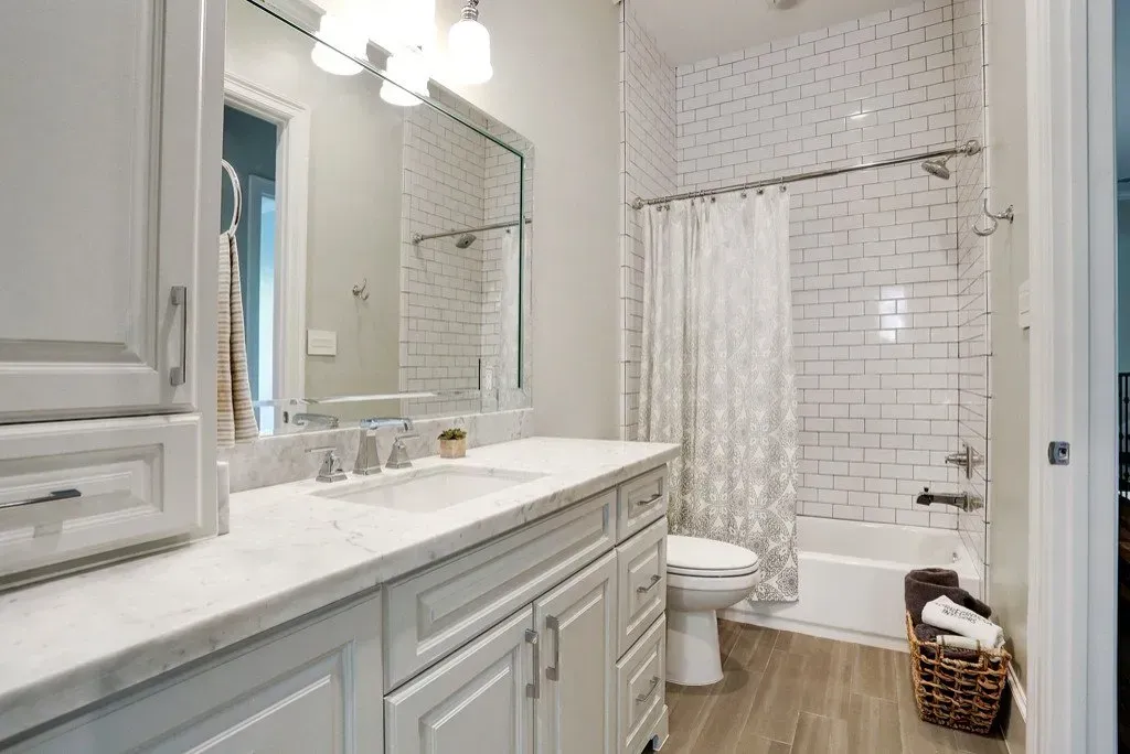 Bathroom with white cabinets, marble countertop, and white subway tile in shower.