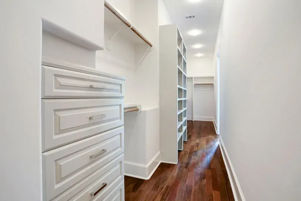 Walk-in closet with white cabinets, shelves, and hardwood floor.