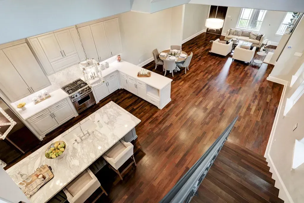 High-angle shot of a modern kitchen with island and dining area, hardwood floors, and a living room.