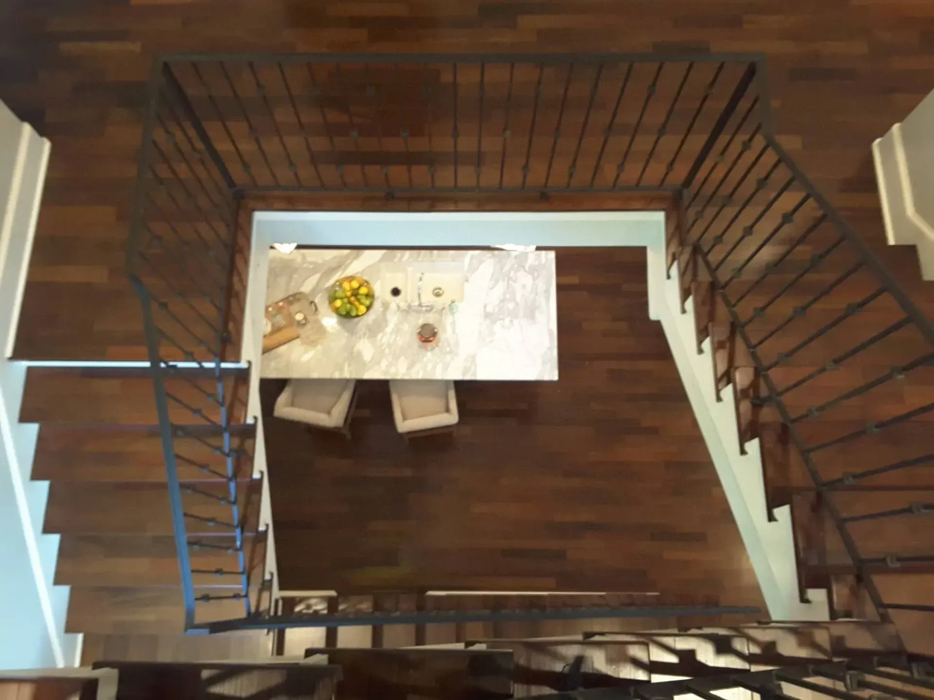 Overhead view of a dining table with chairs, nestled between two staircases with wood treads and black metal railings.