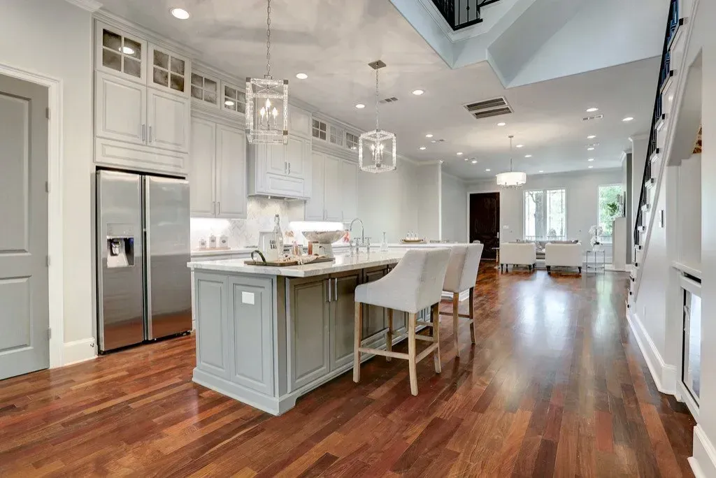 A modern kitchen with a large island, wood floors, and connected dining area.