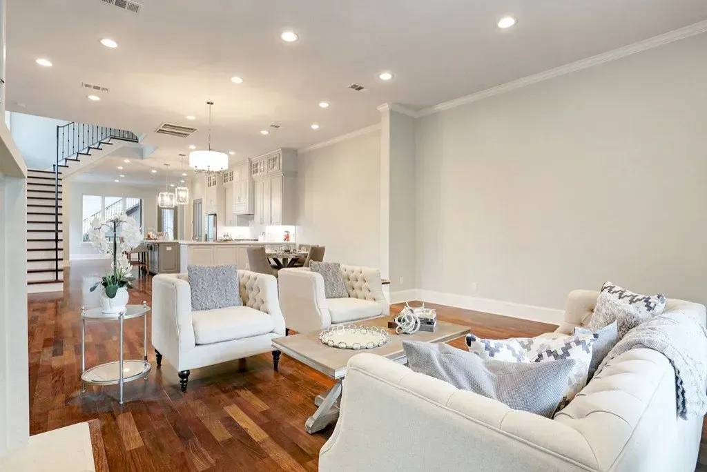 Spacious living room with white couches, hardwood floors, and access to a modern kitchen.
