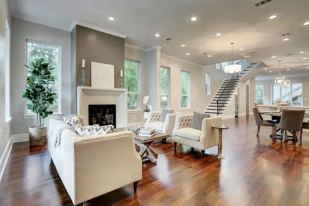 Spacious living room with fireplace, white couches, hardwood floors, and a staircase.