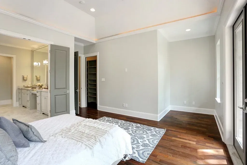 Bedroom with a bed, rug, and access to a bathroom and closet. Hardwood floors and gray walls.