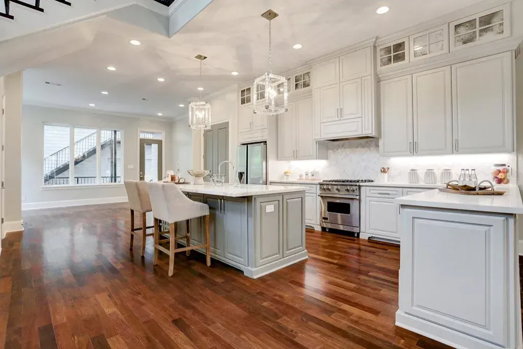 Bright kitchen with white cabinets, gray island, hardwood floors, and modern light fixtures.