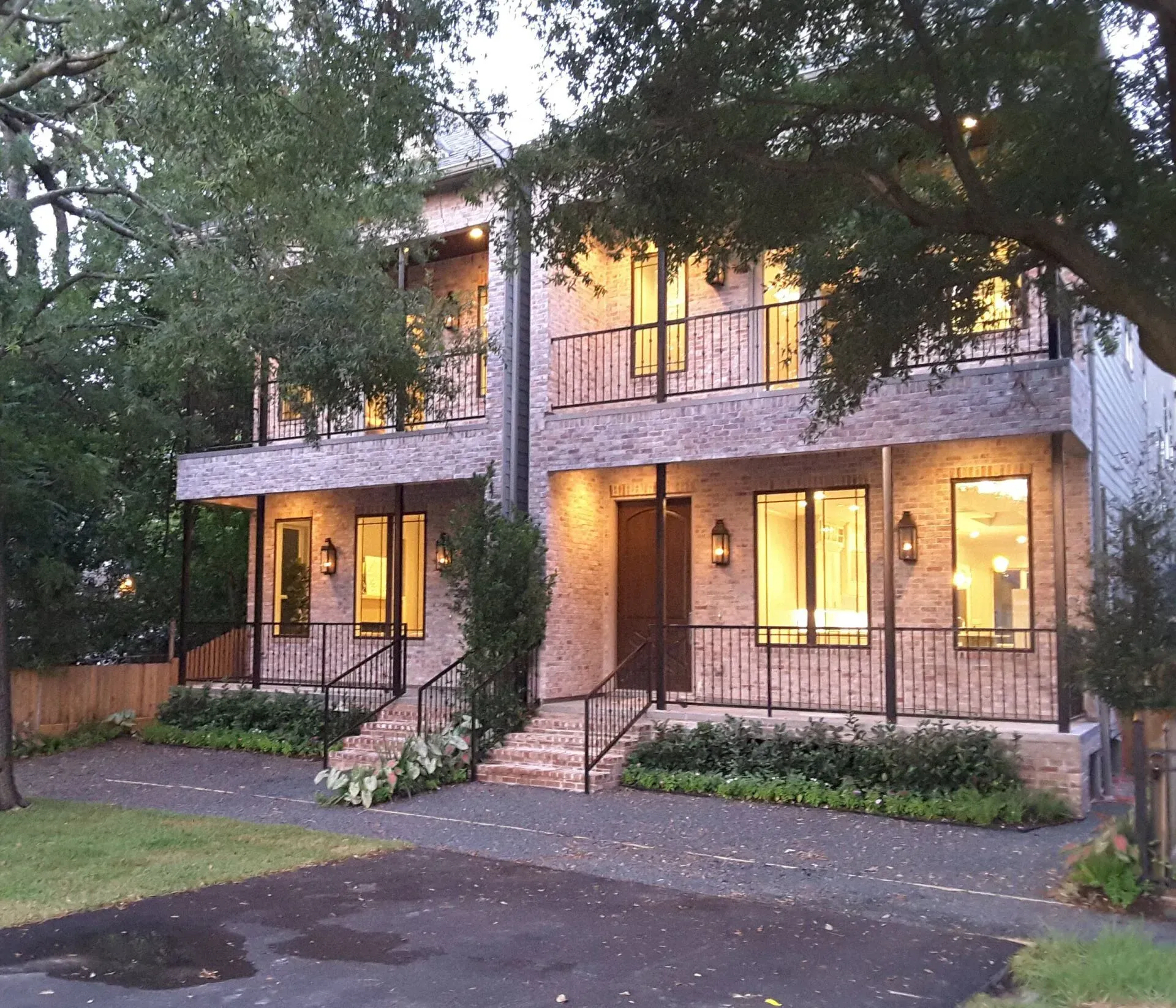 Two-story modern brick townhomes with balconies, lit windows, and dark metal railings.