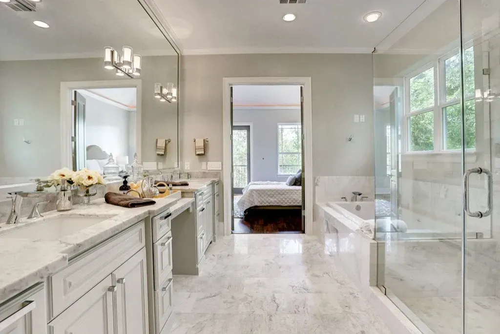 Bathroom with white marble floor and countertops, glass shower, and view into the bedroom.