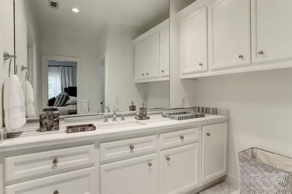 White bathroom with vanity, cabinets, mirror, and a glimpse into a bedroom.