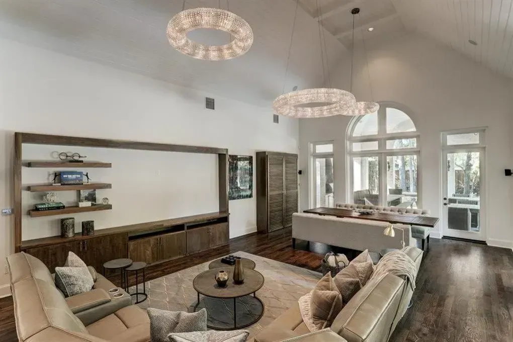Spacious living room with wood furniture, large windows, vaulted ceiling, and two decorative circular lights.
