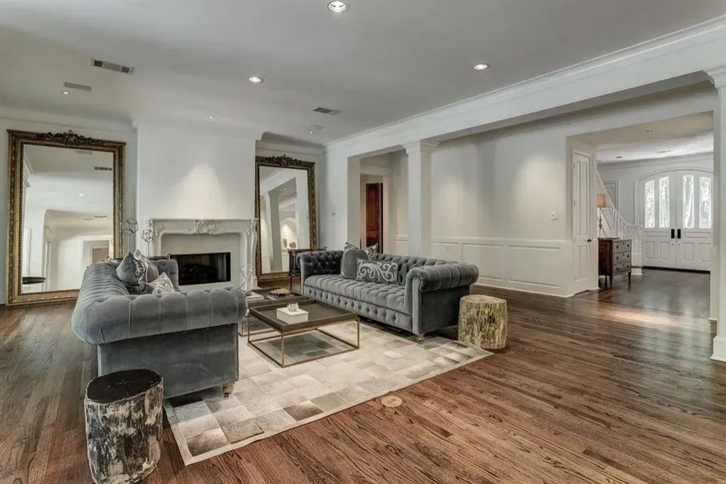 Living room with hardwood floors, two velvet sofas, large mirrors, fireplace, and light-colored walls.