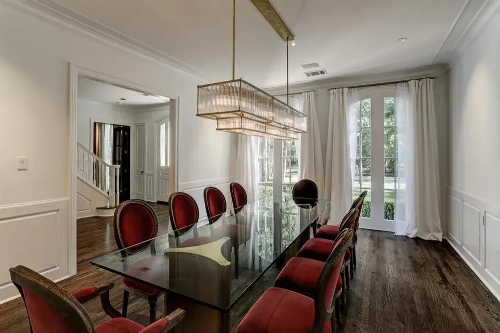 Elegant dining room with red chairs, glass table, and chandelier.
