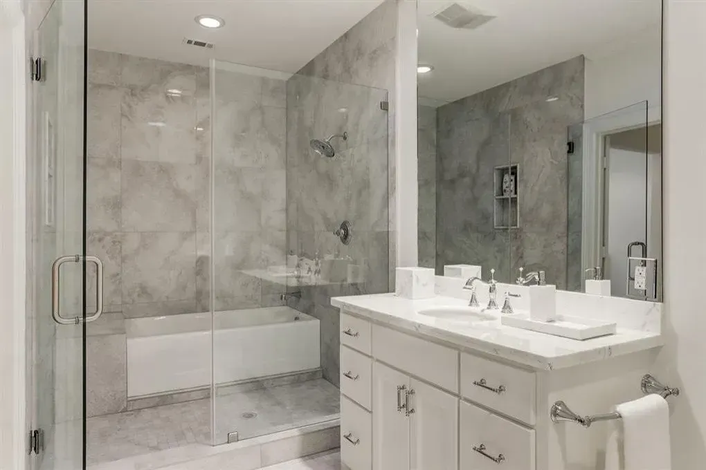 Bathroom with marble walls, glass shower, white vanity, and large mirror.