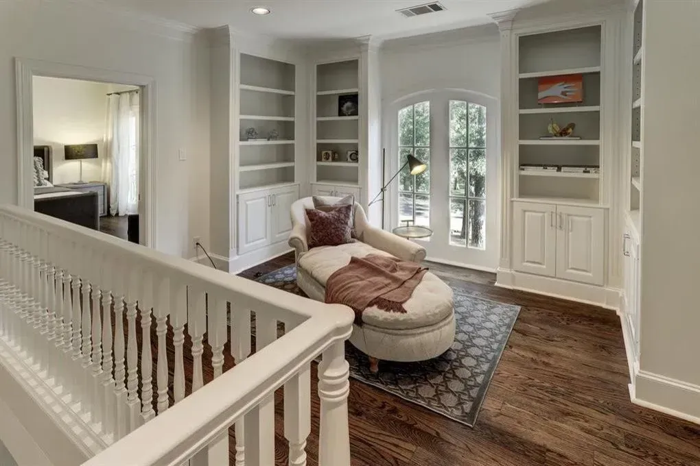A reading nook with built-in bookshelves, a chaise lounge, and double doors to a balcony, white walls and wooden floors.
