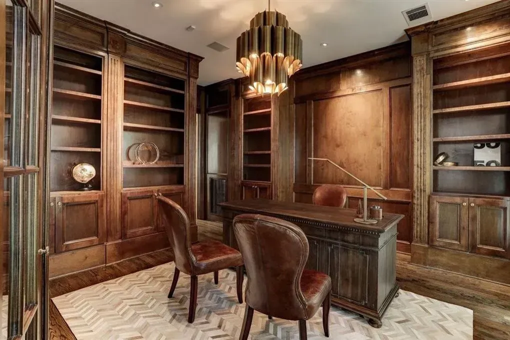 Wood-paneled office with built-in bookshelves, dark desk, leather chairs, and a gold light fixture.