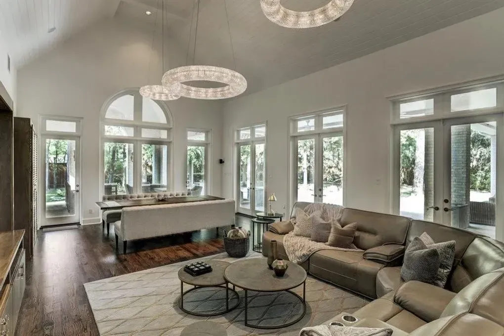Spacious living room with large windows, neutral colors, modern furniture, and a vaulted ceiling.