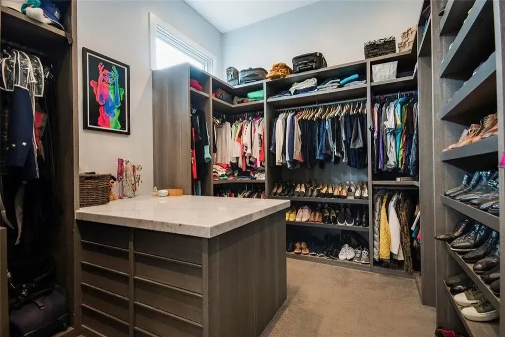 Walk-in closet with gray cabinets, hanging clothes, and a center island with a white countertop.