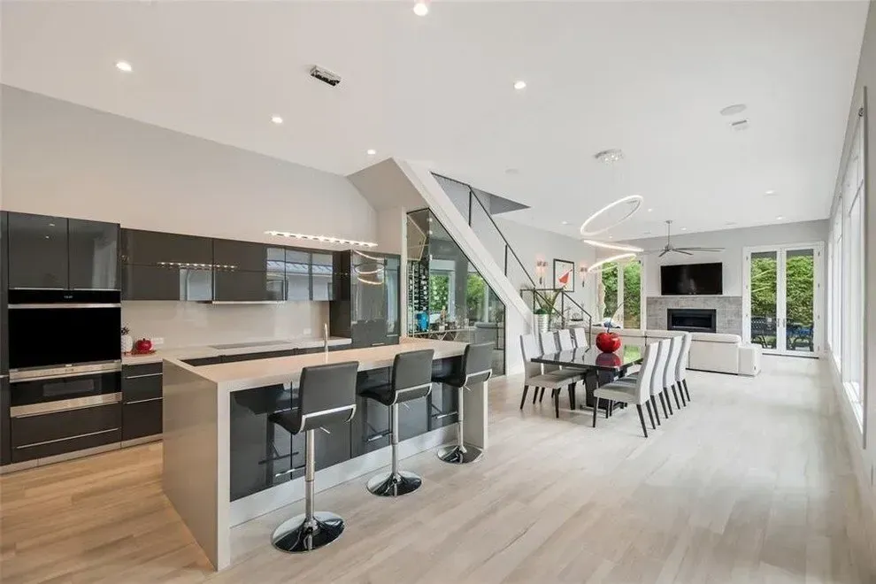Modern open-plan kitchen and dining area with high ceilings, gray cabinetry, and a light wood floor.