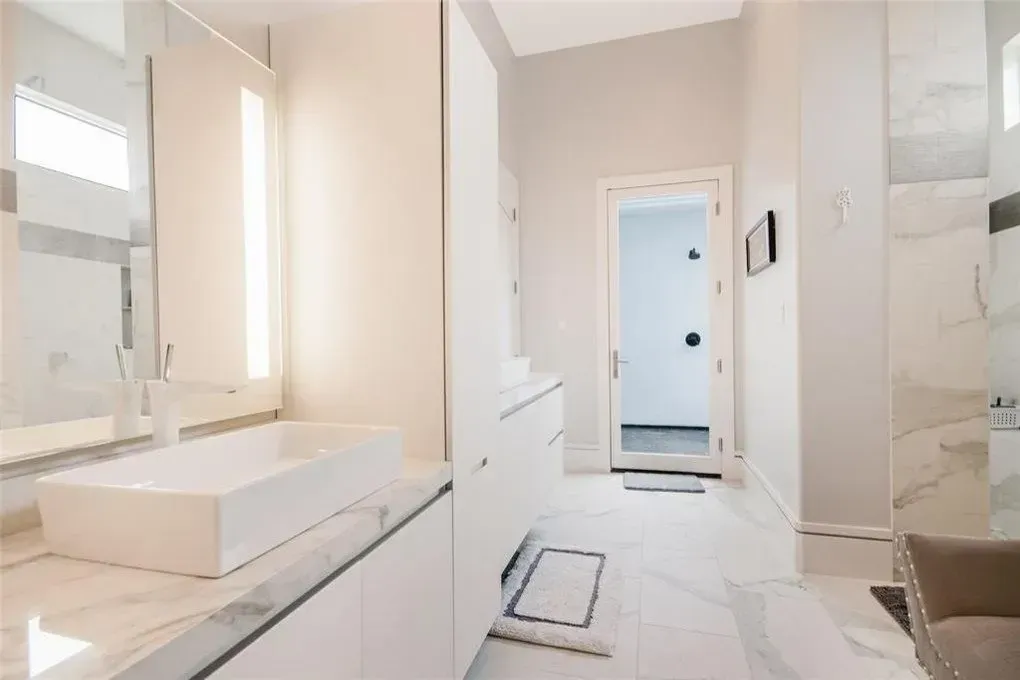Modern white bathroom with marble countertop and floor, and an open doorway.