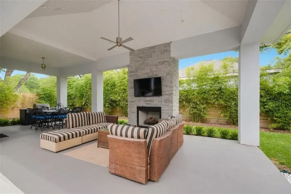 Covered patio with seating, fireplace, and TV. Green trees in the background.