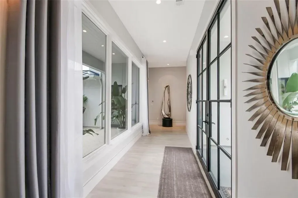 Hallway with windows on the left, a dark framed door, and a sunburst mirror. Neutral colors and natural light.