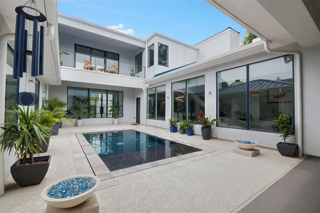 White modern house with a pool, plants, and large windows. Sunny outdoor patio.
