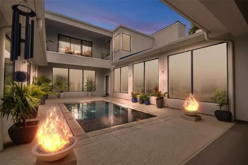 Modern home exterior with a pool, two fire pits, and large windows at dusk.