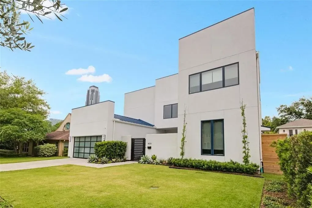 Modern white house with flat roofs, green lawn, blue sky.