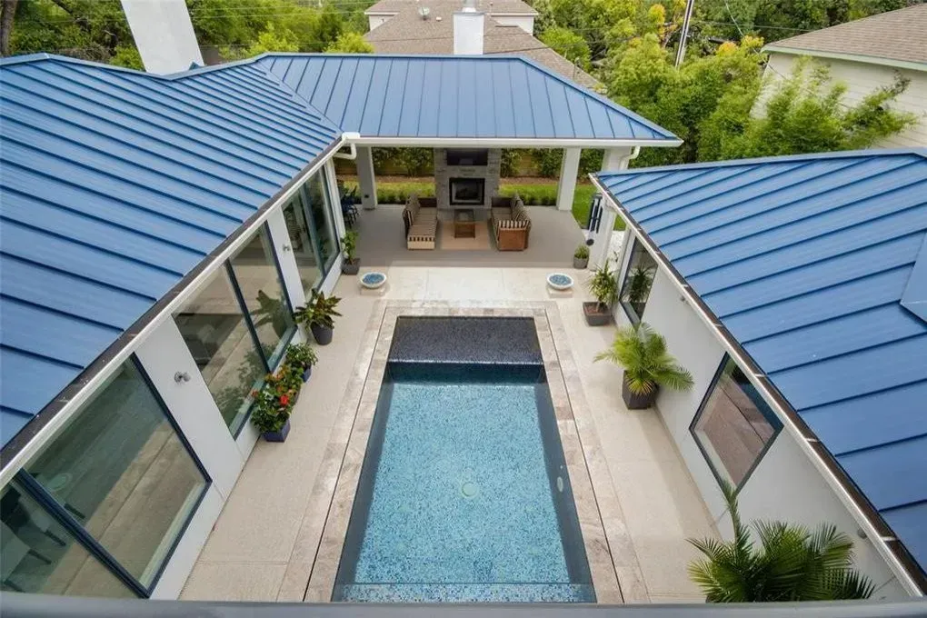 Overhead view of a modern home with a blue metal roof, pool, and patio with seating.
