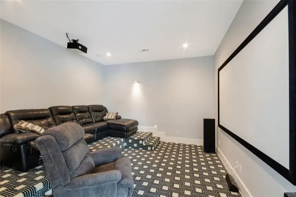 Home theater with black leather sectional, gray recliner, projection screen, and geometric carpet.